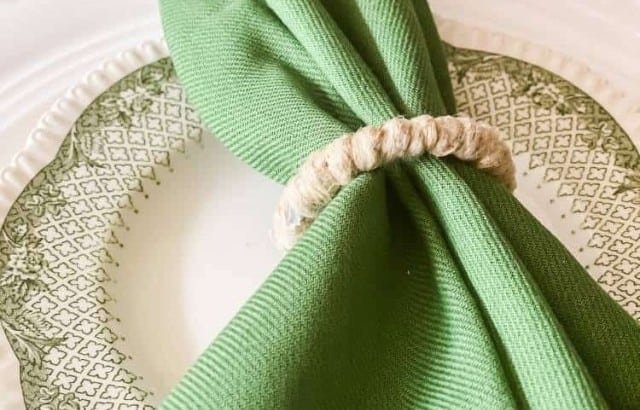 Close up of a table place setting focusing on a green transferware plate and green cloth napkins held with jute napkin rings