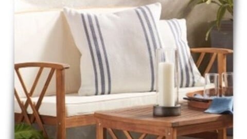 Outdoor living space with teak wood bench and table, ticking striped pillows, and blue rug