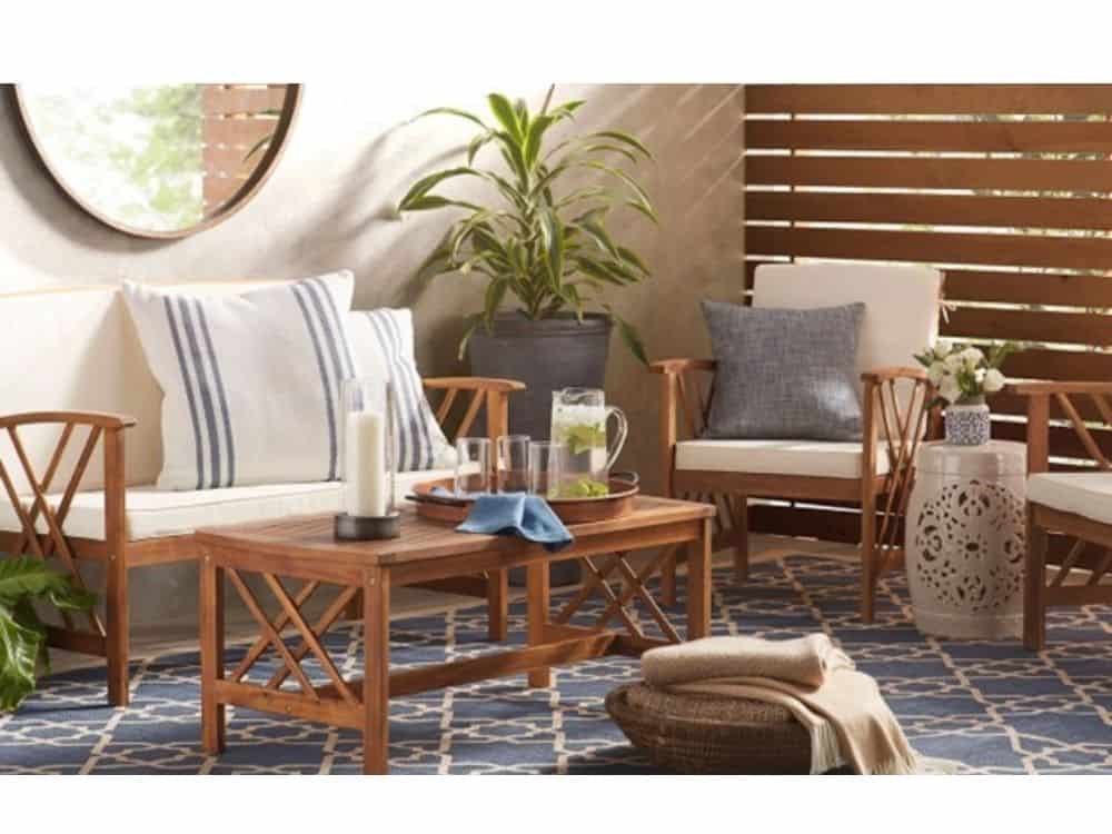 Outdoor living space with teak wood bench, chairs, and table, ticking striped pillows, and blue rug