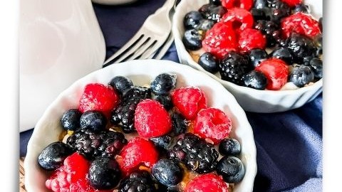 Two mini fruit pizzas topped with mixed berries on a tray with forks and a carafe