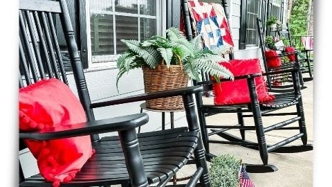 Black rocking chairs on a porch with red throw pillows and basket of ferns
