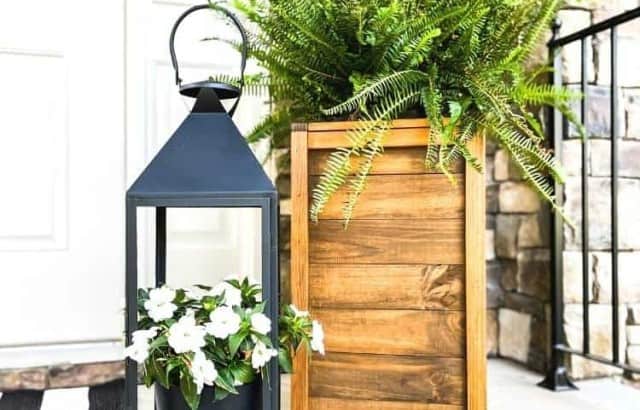 wood planter box with fern behind metal lantern with flowers on porch