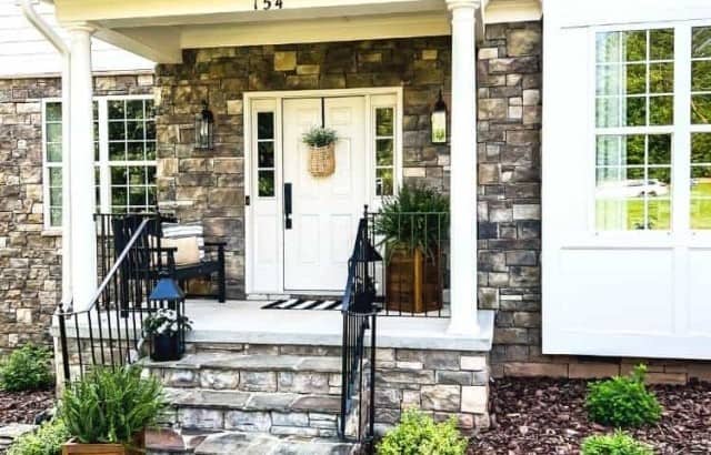 small covered porch in front of white house with stone front