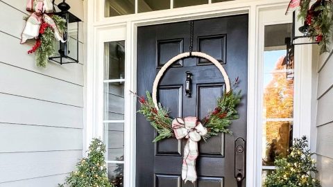 Black front door with side lights decorated for Christmas with a large hoop wreath