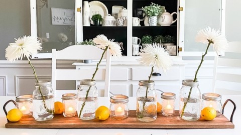 Wood tray with mason jar vases of white flowers, lemons, votive candles on a dining room table