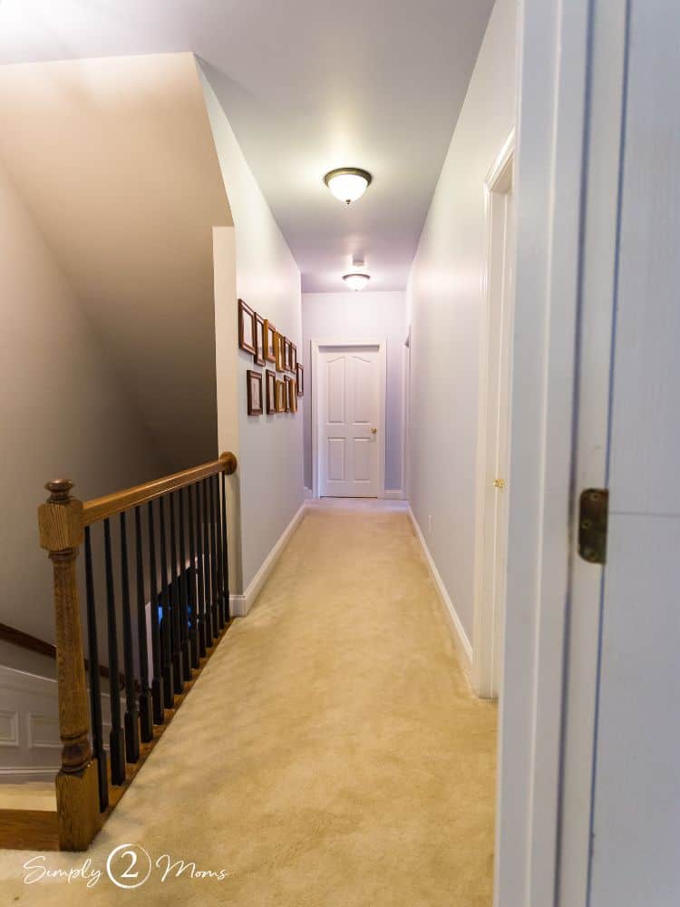 Dark and narrow upstairs hallway with stair railing, carpeting, gallery wall, and boob lights.