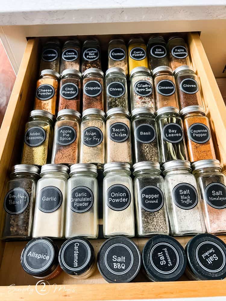 Drawer with rows of glass spice jars with round printed black labels.