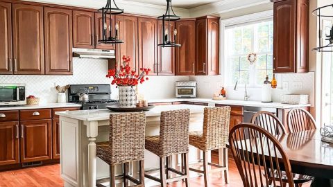 Kitchen with cherry cabinets and white quartz counters, white island, and white backsplash. and rattan counter stools.