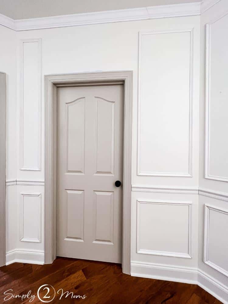 Interior door and frame painted Revere Pewter in a white hallway with picture frame molding, chair railing, and crown molding.