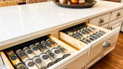 Two drawers in a kitchen island are open to reveal organized matching spice jars with round black printed labels.