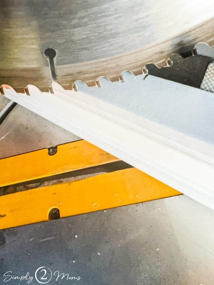 A piece of trim sitting upright on the table of a miter saw to show where to position the saw blade on a measuring mark.
