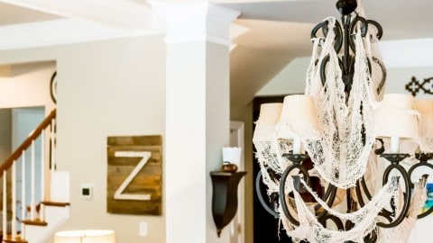 Black metal chandelier with lamp shades decorated for Halloween with strips of cheese cloth.