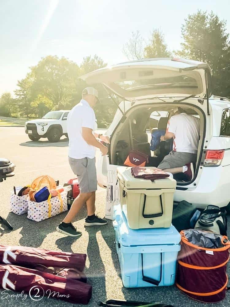 Two men unloading gear from the back of a mini van for a tailgate party.