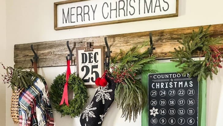 Row of farmhouse hooks decorated for Christmas with signs, advent chalkboard, basket, stocking, and greenery.