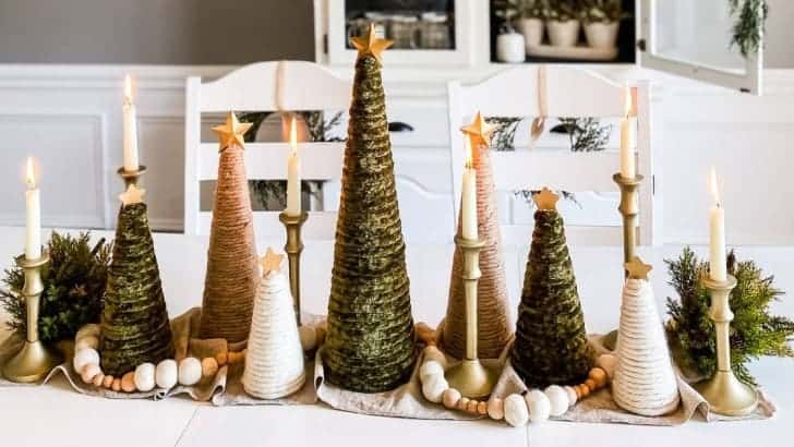 Neutral Christmas centerpiece with three colors of yarn-wrapped trees, geenery, and candles.