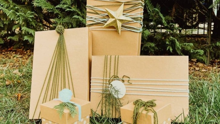 Five Kraft paper boxes of different sizes decorated with green and white yarn tied and wrapped in different ways for Christmas.