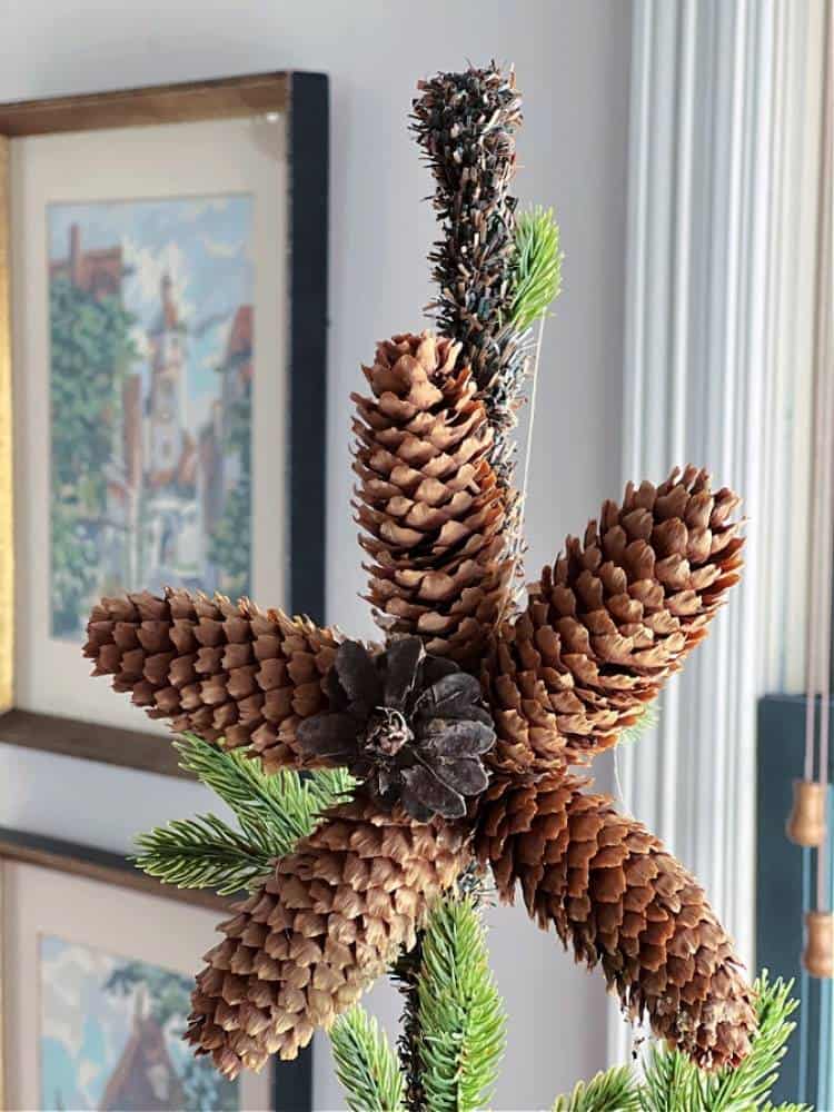 Five-point star made from long skinny pinecones on top of a Christmas tree.