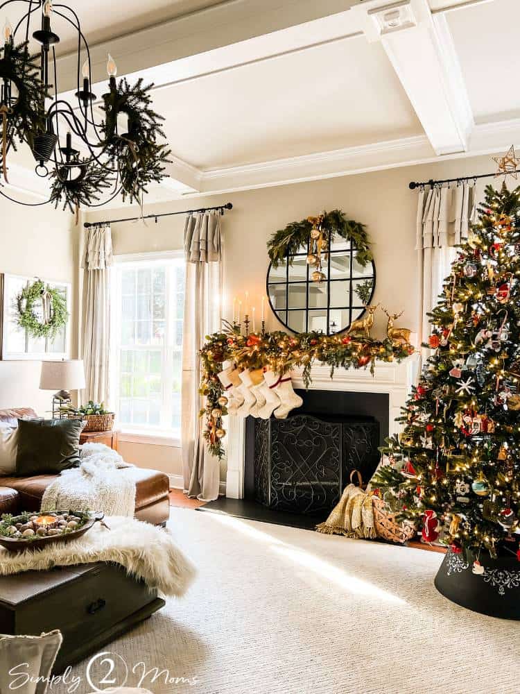Family room decorated for Christmas with a tree, fireplace with greenery, mirror, and wreaths.