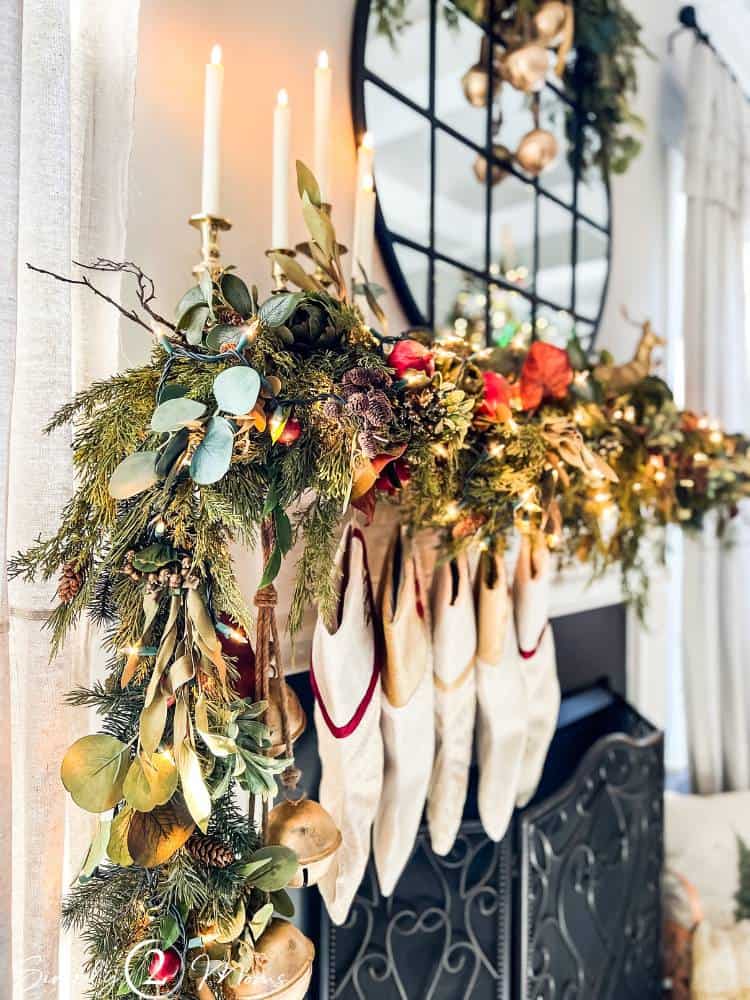 Christmas greenery on a mantle with stockings, twinkle lights, and tapers in brass candlesticks.