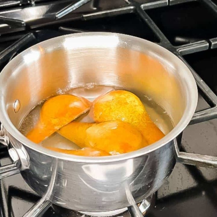 Black gas stove with a stainless steel saucepan with quartered pears in simple syrup.