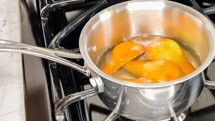 Black gas stove with a stainless steel saucepan with quartered pears in simple syrup.