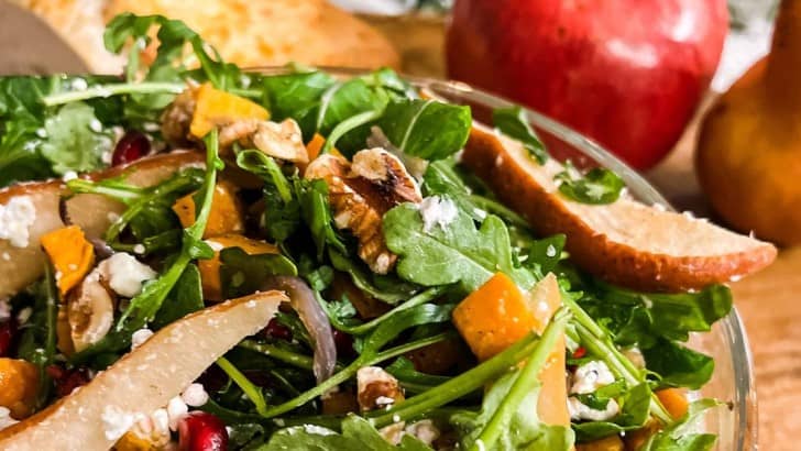Bowl of winter salad with sliced pears, pomegranates, sweet potato, walnuts and goat cheese.