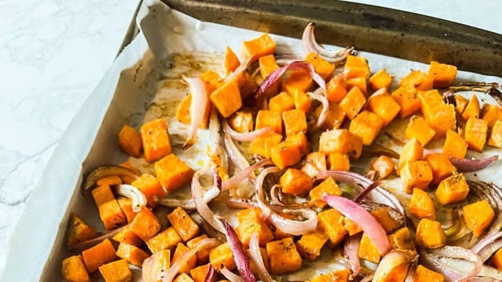 Baking sheet lined with parchment paper with roasted sweet potato cubes and sliced red onions.