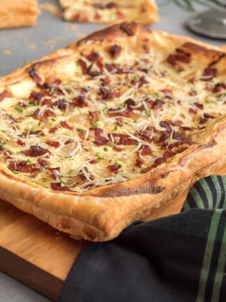 Bacon and cheese onion tart on a wood board with a plaid napkin.