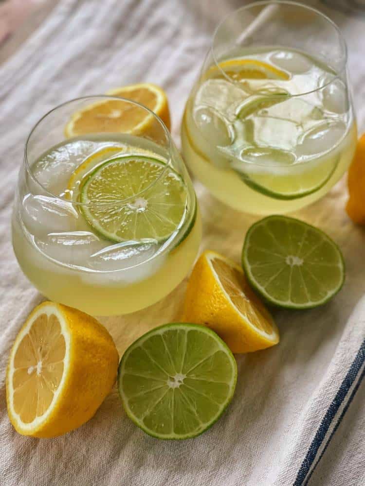 Two stemless glasses with citrus wine spritzers on ice with cut lemons and limes.