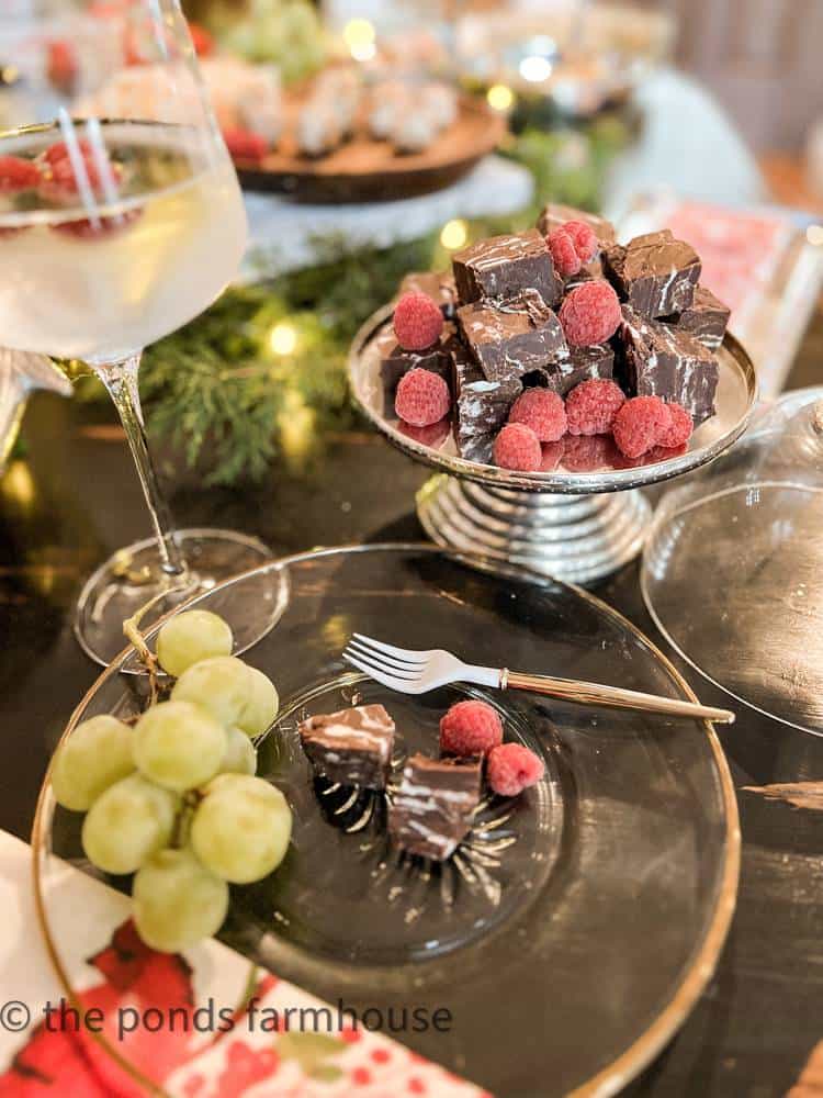 Glass plate with serving of dark chocolate raspberry fudge next to a serving plate of the dessert.