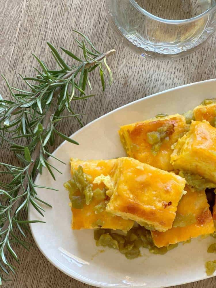 Squares of green chile cheese fudge stacked on a plate with a sprig of fresh rosemary.