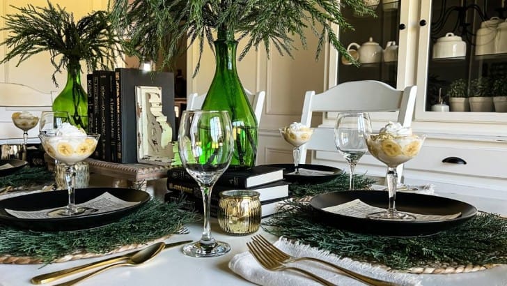 Dining table set with black plates with parfait glasses of banana pudding on top of each place settings.