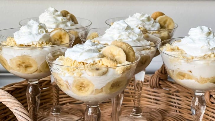Stemmed dessert glasses with easy boozy banana pudding parfaits garnished with whipped cream and banana slices.