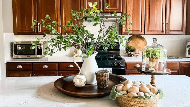 Kitchen island with large wood bowl centerpiece with white vase filled with spring branches and basket of wood eggs.