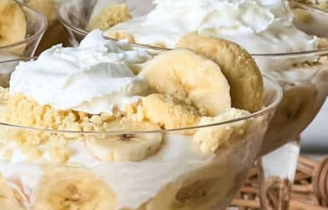 Stemmed dessert glasses with easy boozy banana pudding parfaits garnished with whipped cream and banana slices.