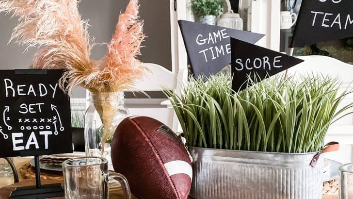 Table decorated with an old football, container of faux grass, and black chalkboard signs with football sayings.