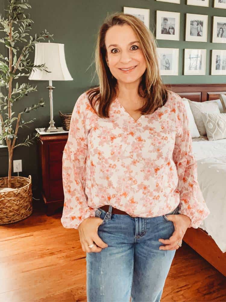 Woman wearing a long sleeve v-neck blouse with a pink and orange floral print on a white background.
