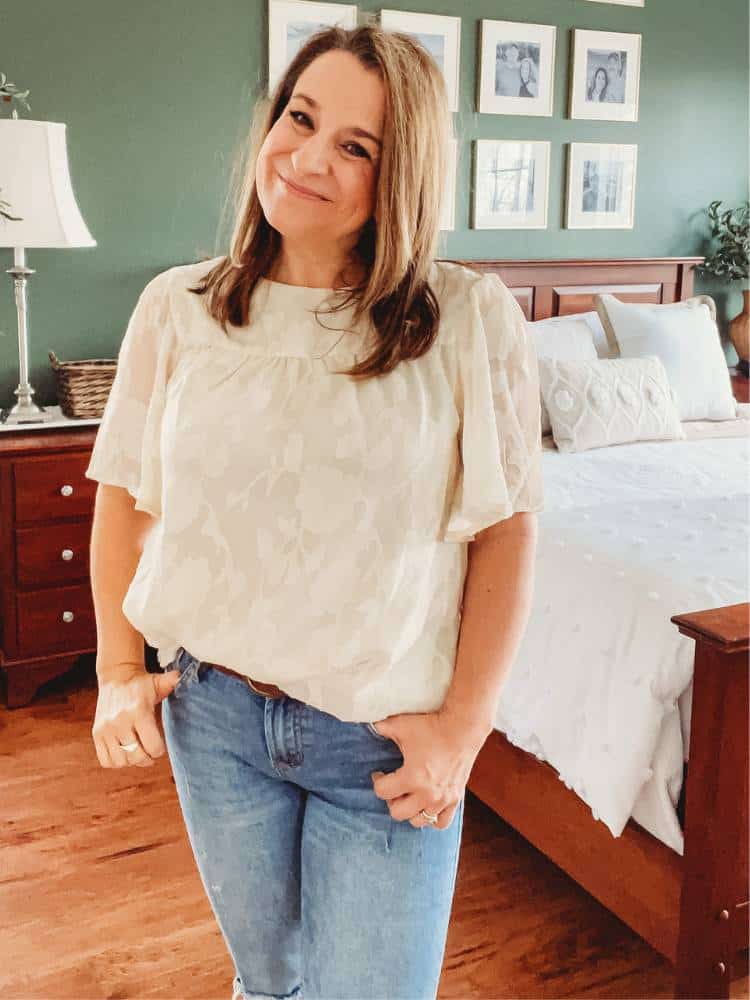 Woman wearing a cream short sleeve shirt with a floral pattern texture.