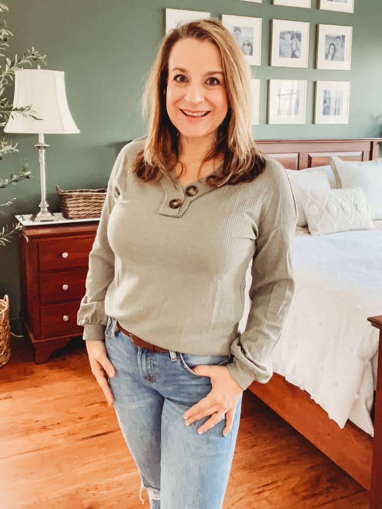 Woman wearing a waffle knit V neck top with long bloused sleeves. There are large buttons on one side of the neckline.