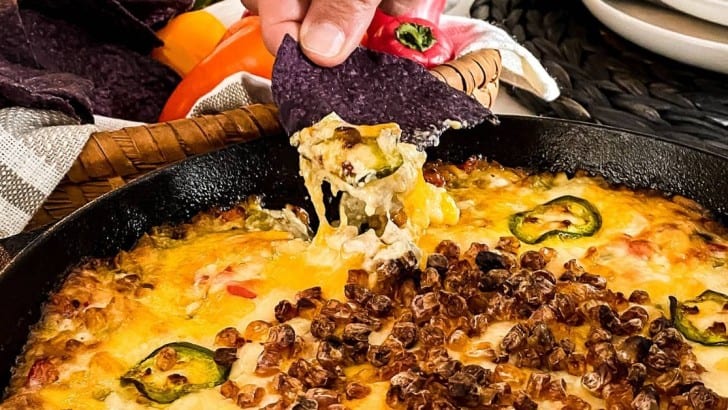 Blue corn tortilla chip dipping into a cast iron pan filled with Hot Roasted Corn Dip.