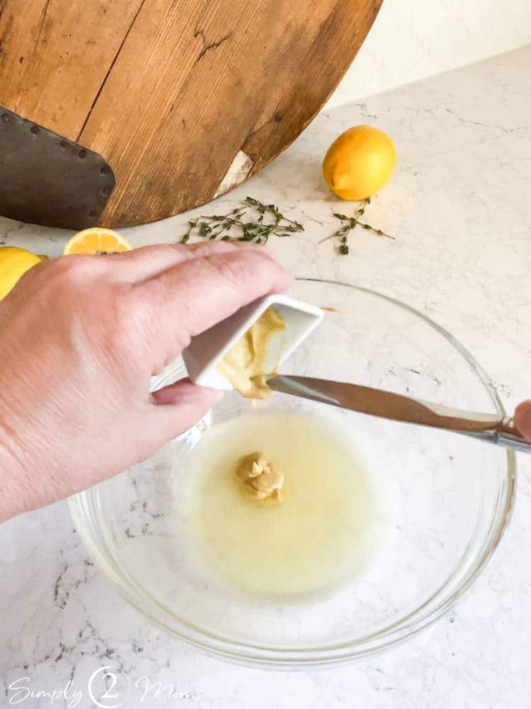 Small glass bowl of fresh lemon juice and small ramekin of Dijon mustard being added.