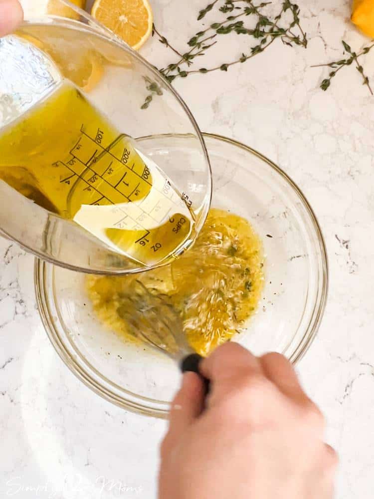 Sweet lemon vinaigrette dressing in a small glass bowl with olive oil being poured in and whisked.