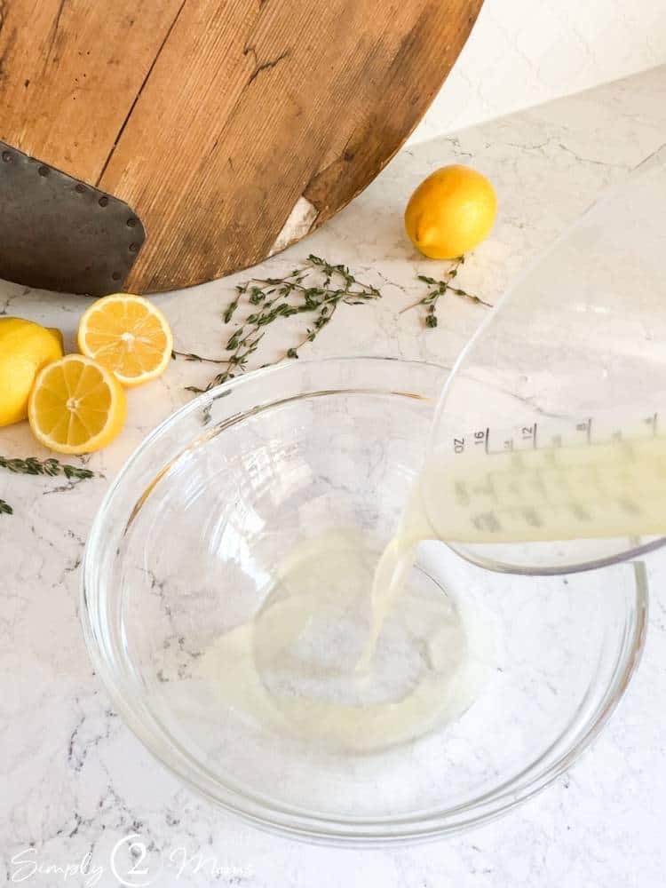 Small glass bowl with a measuring cup of fresh lemon juice pouring in to make dressing.