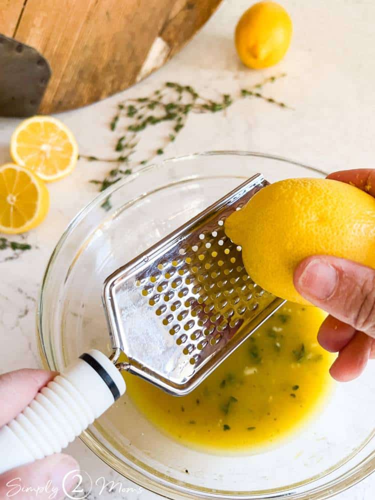 Sweet lemon salad dressing in a bowl while someone grates the zest from a fresh lemon.