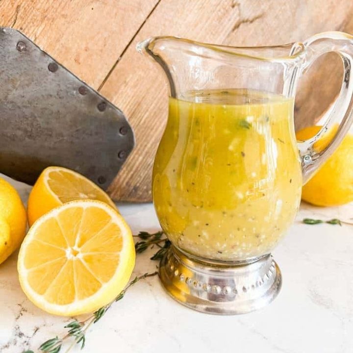 Small glass pitcher filled with sweet lemon vinaigrette dressing with fresh lemons.