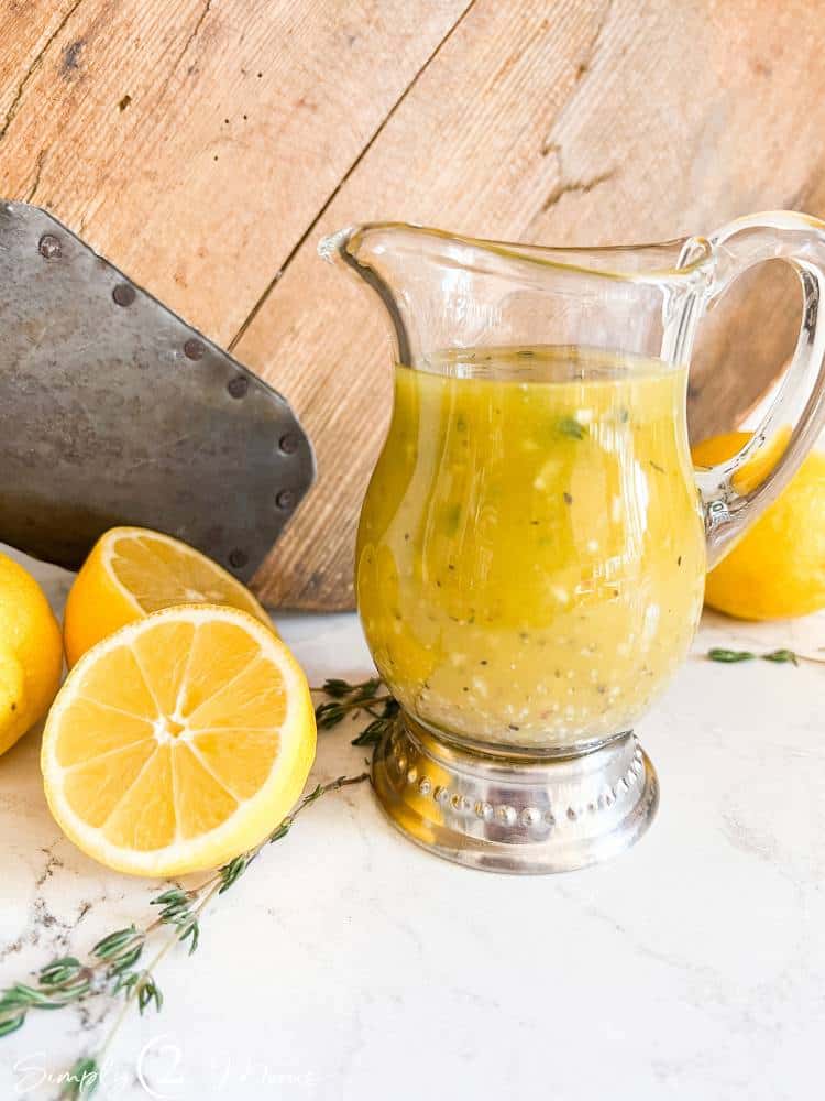 Small glass pitcher filled with sweet lemon vinaigrette dressing with fresh lemons.