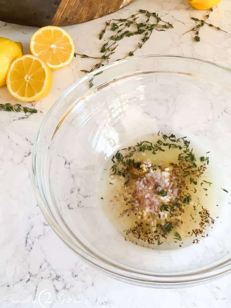 Small glass bowl with lemon juice, seasonings, fresh herbs, minced garlic, and minced shallots.