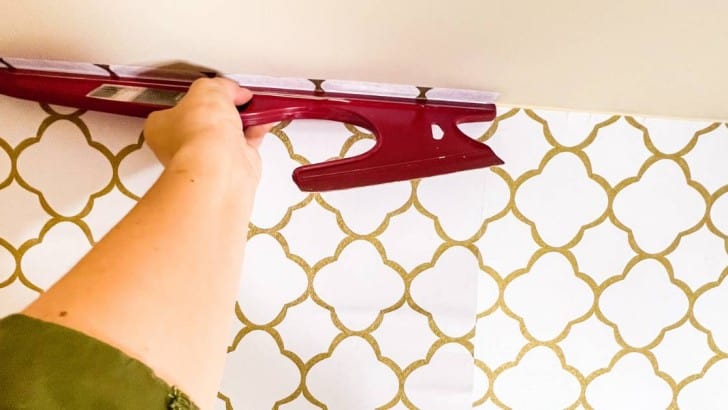 Woman holding a smoothing tool to install peel and stick wallpaper.