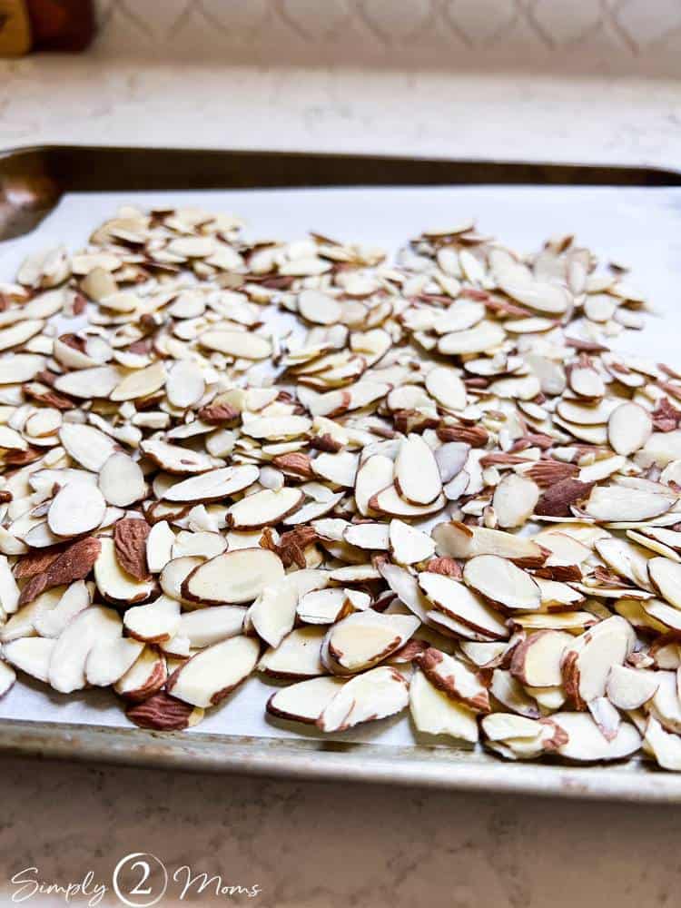 Baking tray lined with parchment paper with sliced almonds spread in a layer.