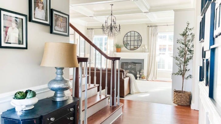 Family room with coffered ceiling and gas fireplace decorated for spring with drop cloth curtains, greenery, and white accents.